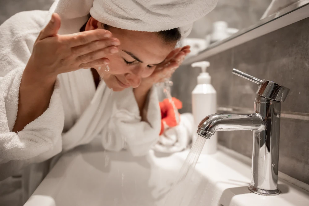 Perempuan mencuci muka dengan air mengalir di wastafel kamar mandi
